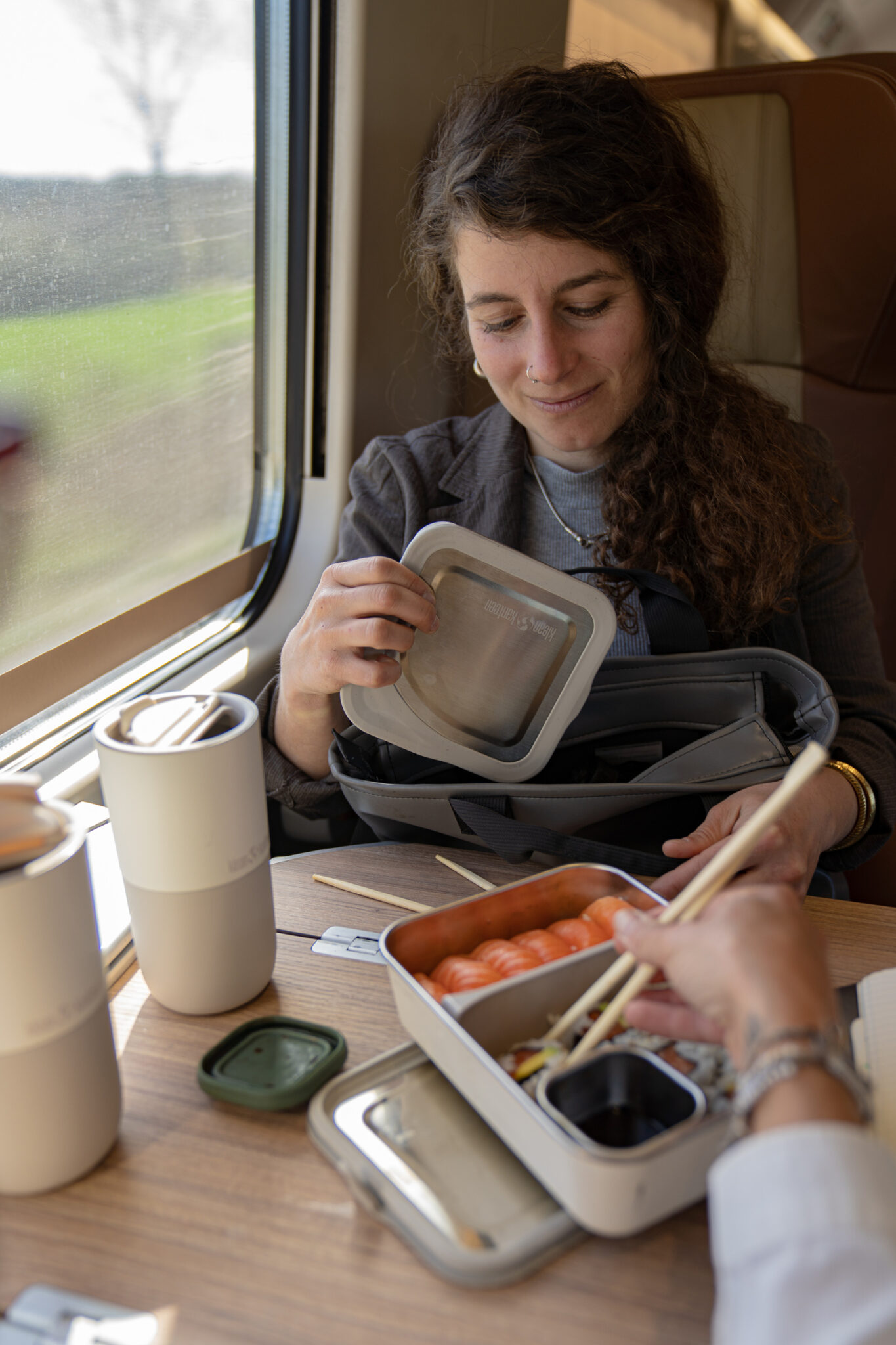 A woman traveling on a train and eating out of her lunch container.