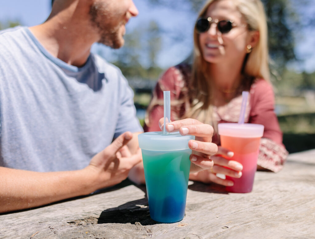 Two people sitting outside holding plastic cups.