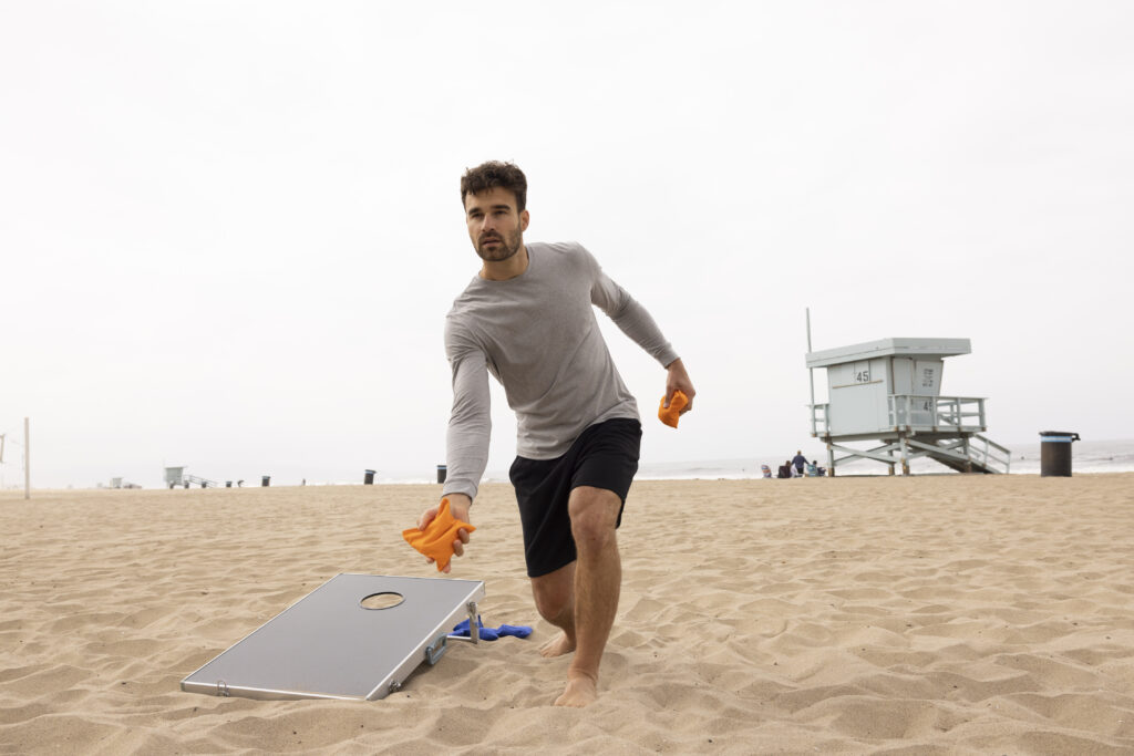 A man playing cornhole on the beach