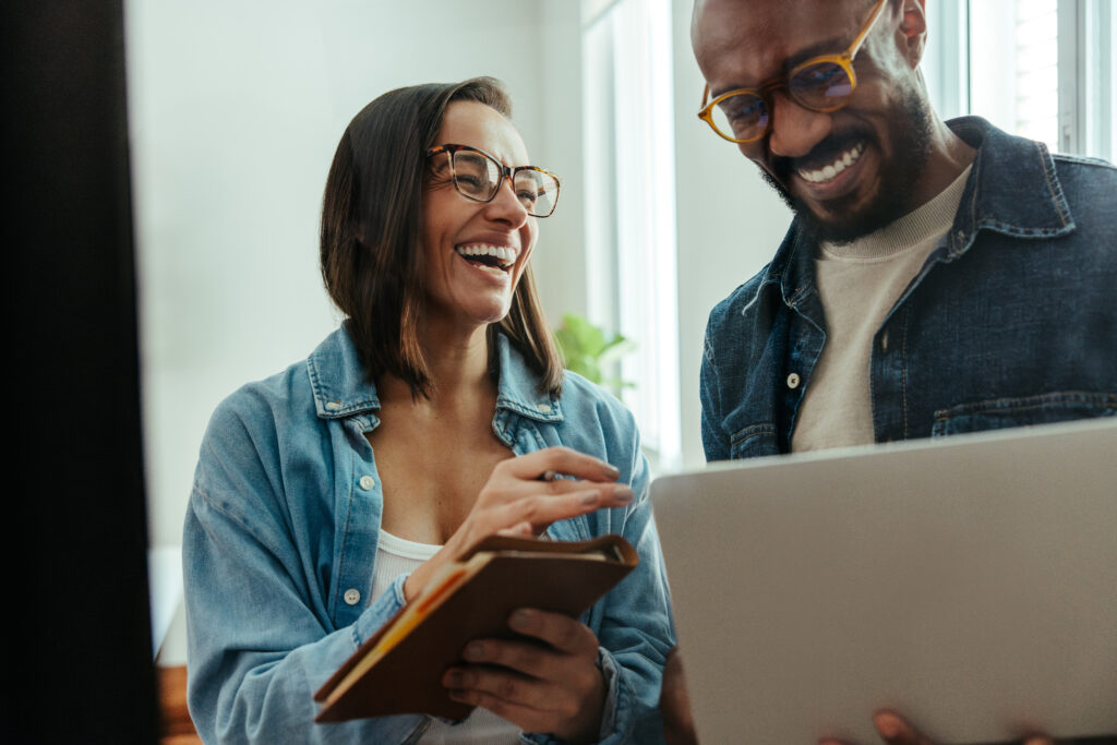 Two happy colleagues laughing and working together on a creative project, showcasing a professional and collaborative office environment.