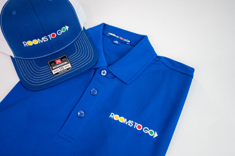 A Rooms to Go branded polo shirt and hat laying flat.