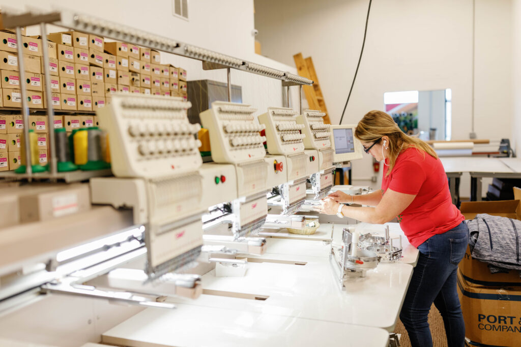 An IDX employee working with an embroider machine to place logos on tee shirts.