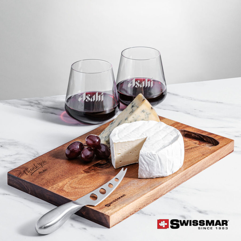 A cutting board with two wine glasses and block of brie cheese and grapes on top.