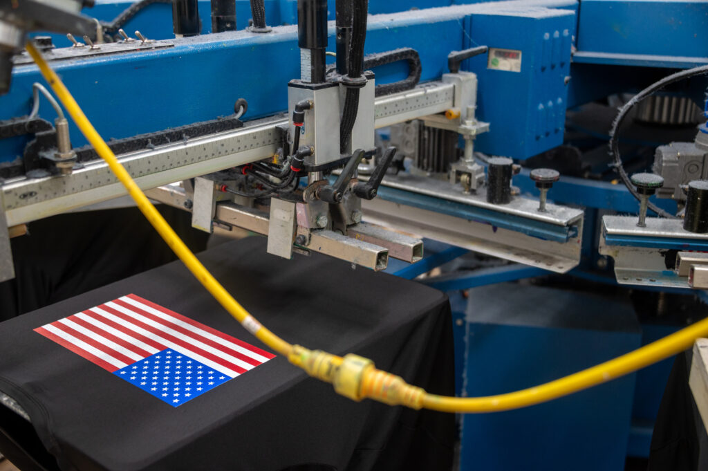 An embroidery machine stitching an American flag on a shirt.