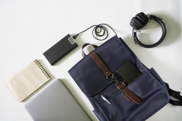 A flat lay of items including a back pack, power bank, notebook, and headphones.