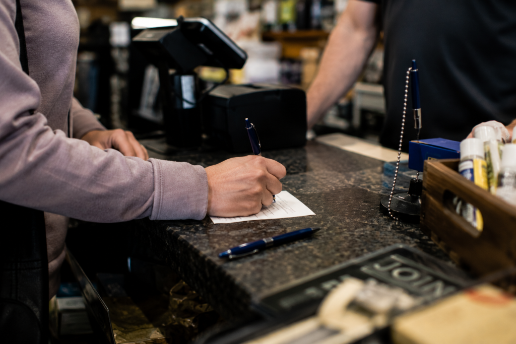 Customer using a pen at a restaurant counter while a staff member looks on
