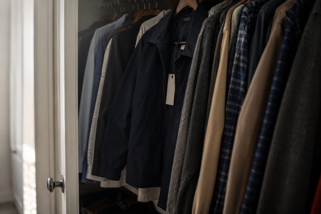 Row of jackets and shirts hanging in a closet, including a navy jacket with a blank hang tag