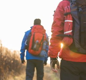 Rear view of male backpackers walking in field.