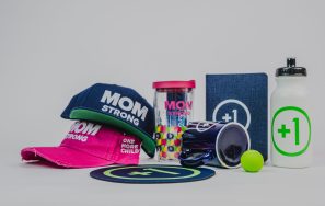 A collection of corporate swag including hats, coffee mug, water tumber, and water bottle, and a notebook for the nonprofit One More Child.