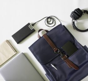 A flat lay of items including a back pack, power bank, notebook, and headphones.